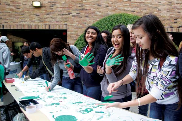 A group of students make the pact to go green by placing their hand-print and signing their name in a banner.