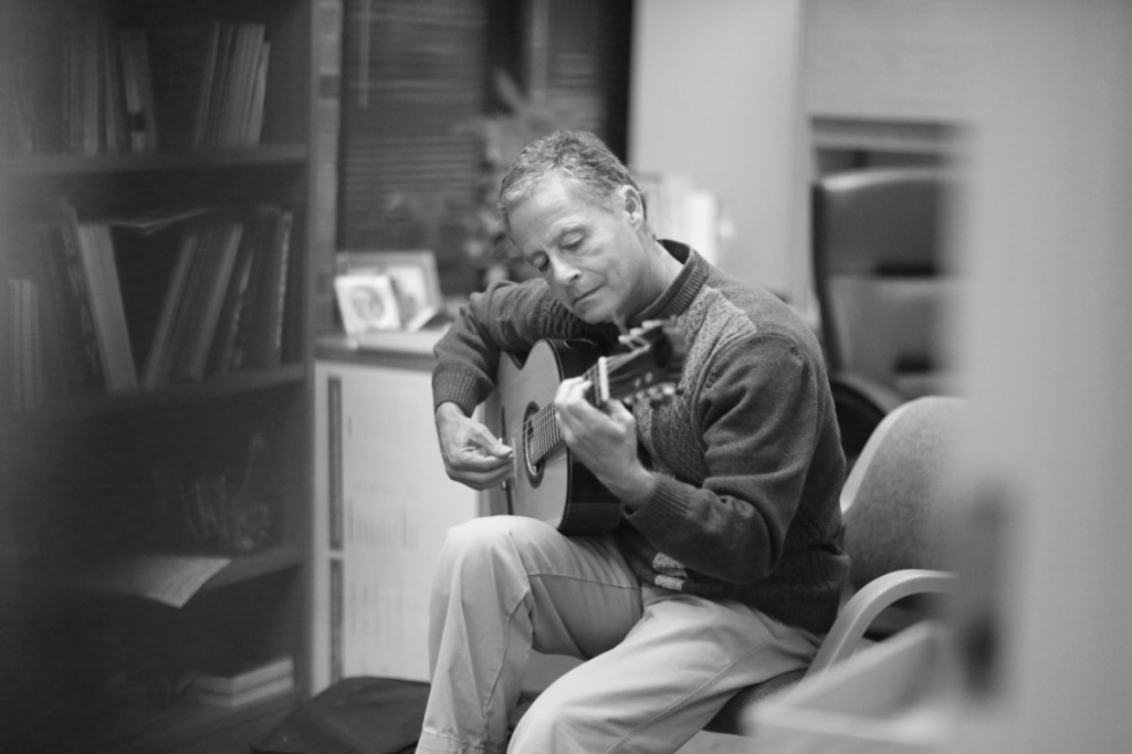 Photo by Adriana Salazar | Rodger Bennett takes a moment to strum a few bars on his guitar in his office.