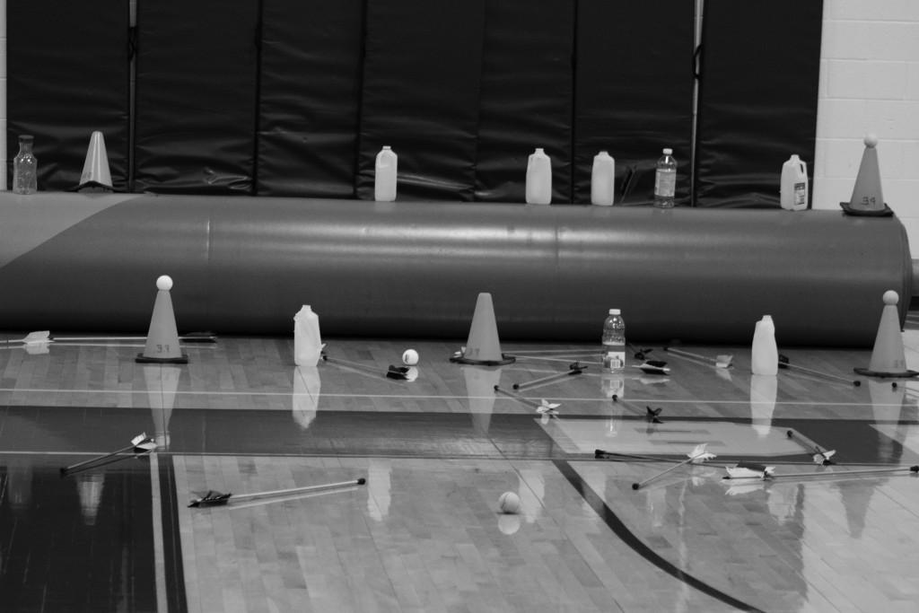 Students practice shooting inside on a cold day using milk containers and road cones with tennis balls as targets.