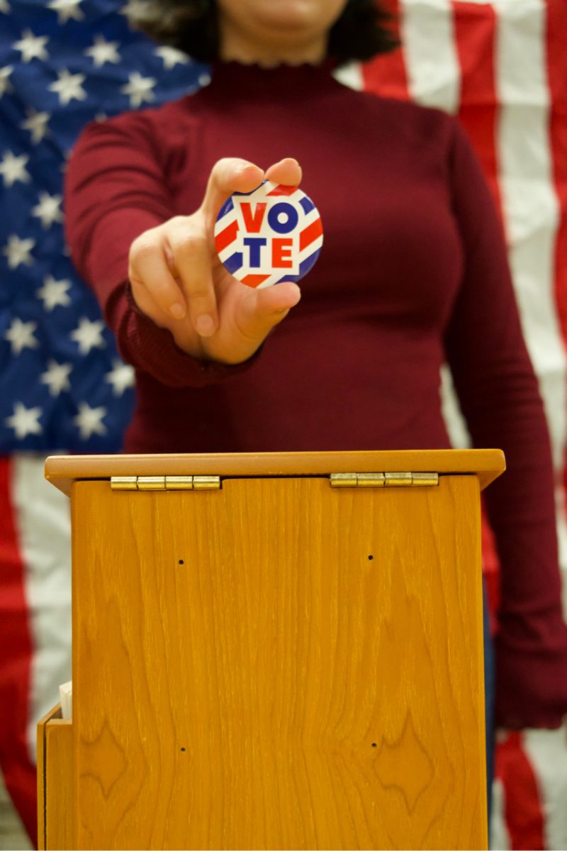 A woman holding a vote pin with an American flag at the background.