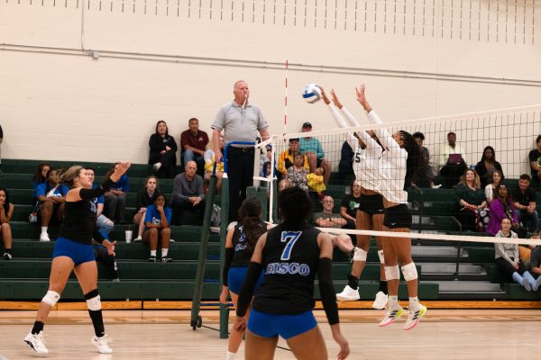 Two women jumping and tossing the ball to the other side of the volleyball net.