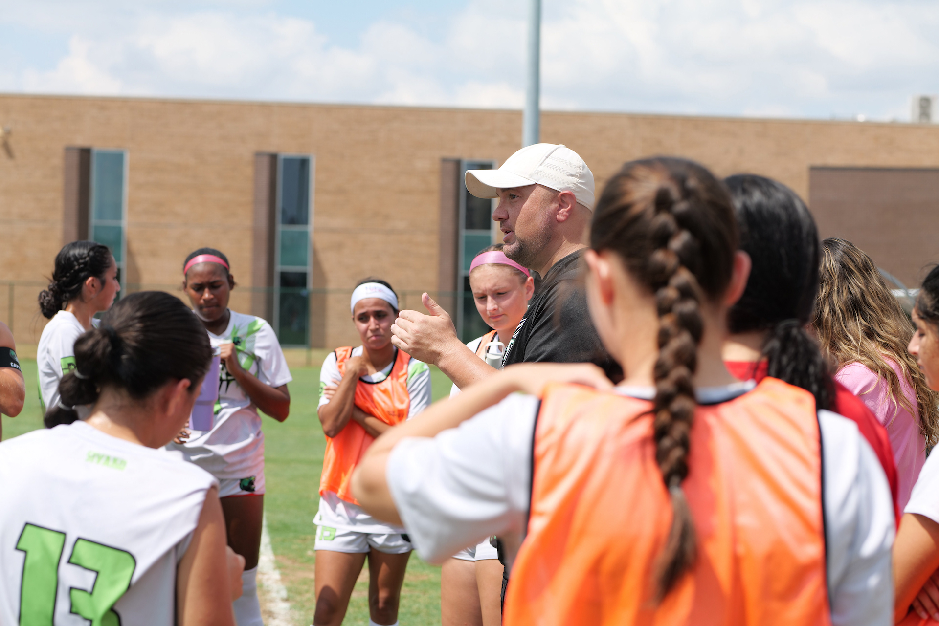 Women soccer players gather around the male coach.