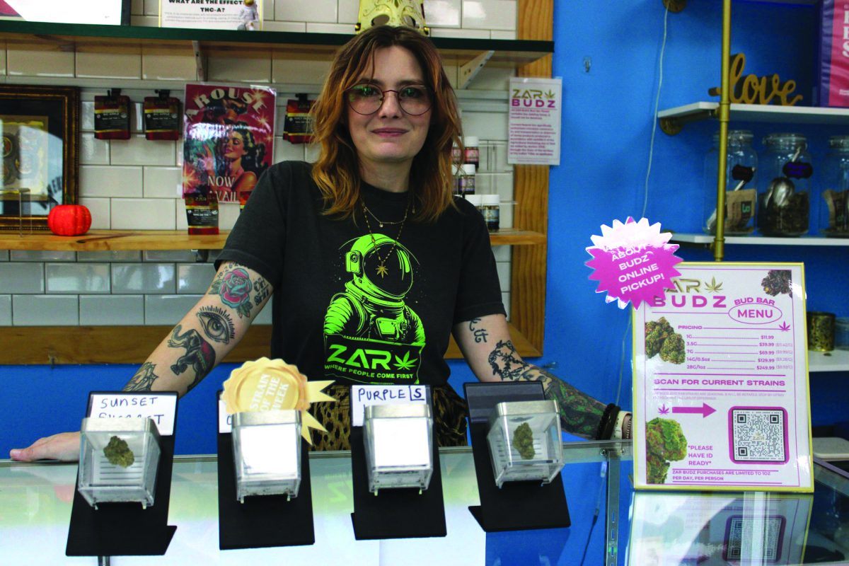 Skye Weatheread, Director of Marketing and Compliance for ZAR, posing next to the bud samples on display at ZAR’s Carrollton location.